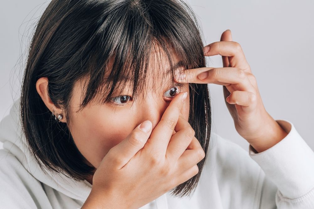 Woman touching her eye with two fingers, checking or applying contact lenses against a light background