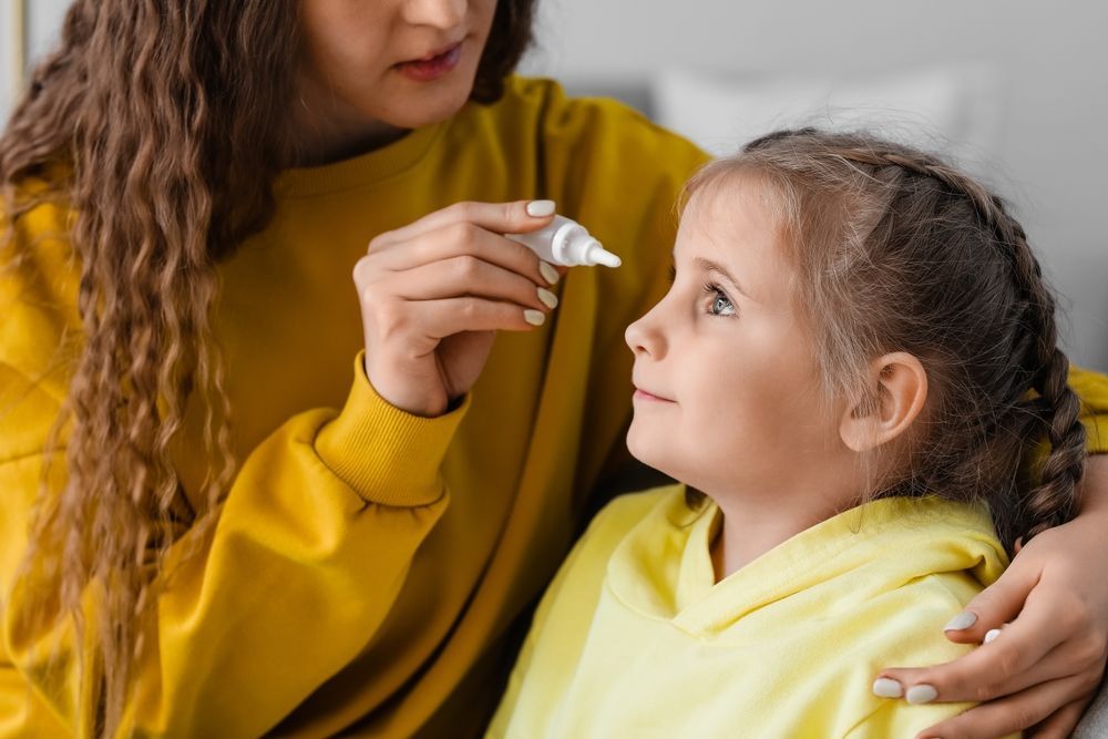 Woman in yellow helping a child with a nasal spray, seated indoors