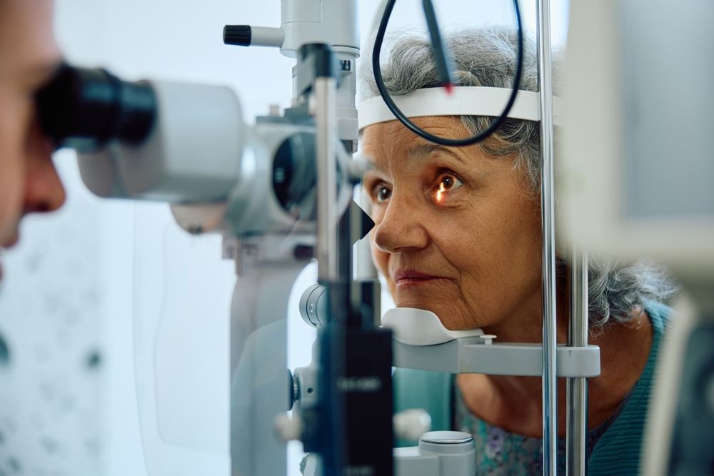 Patient looking into an eye exam machine while an optometrist adjusts the equipment