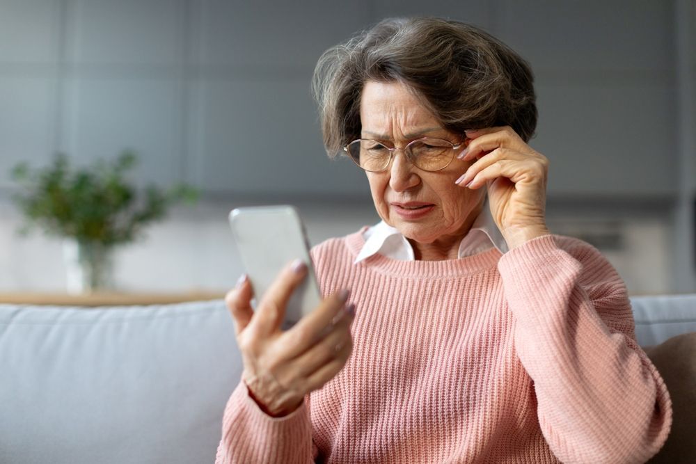 Concerned woman in pink sweater looking at her phone on a couch