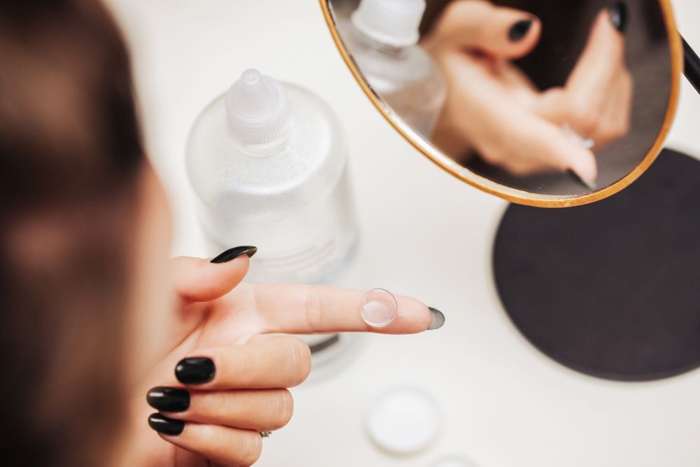 Hand with black nails holding a finger near a white nail polish bottle and manicure tools