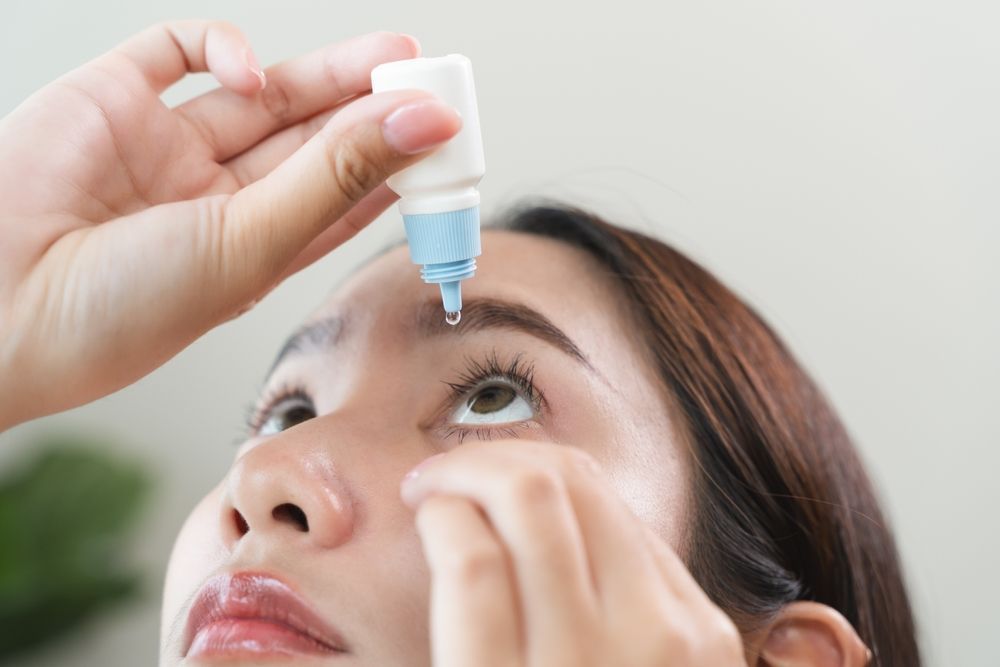 Eye drops being applied to a woman’s eye with a blue bottle, close-up.