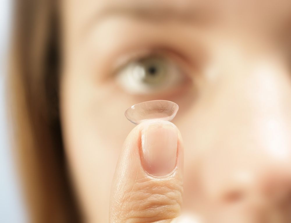 A contact lens held between fingers in front of a blurred face