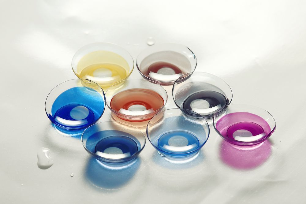 Seven colorful contact lens cases on a white surface, arranged in a cluster.
