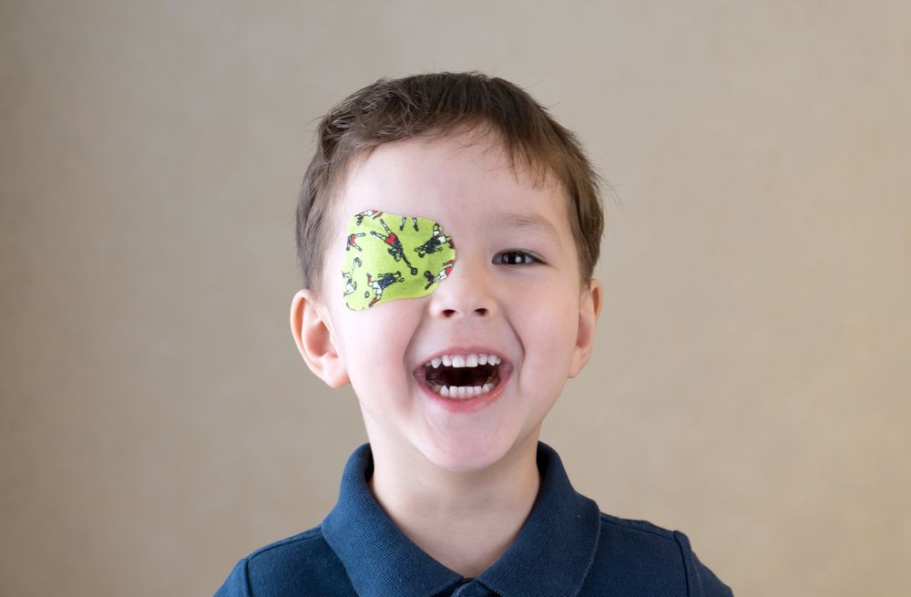 Smiling child with a green eye patch on a plain beige background