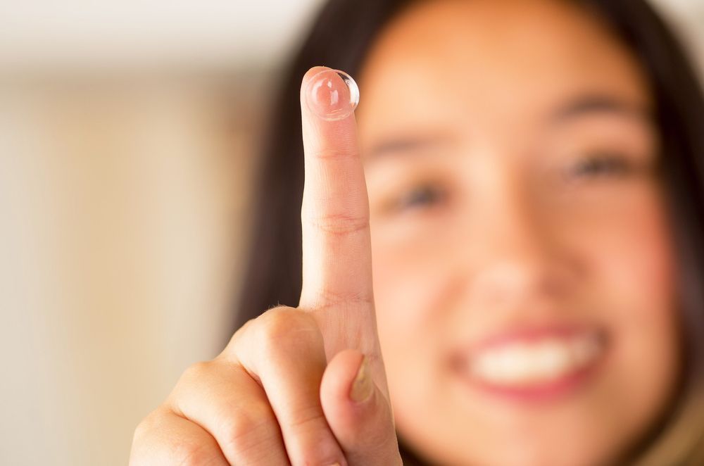 Close-up of a smiling person holding up one finger toward the camera