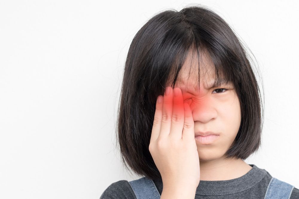 Person holding a red hand to their eye, looking uncomfortable against a white background
