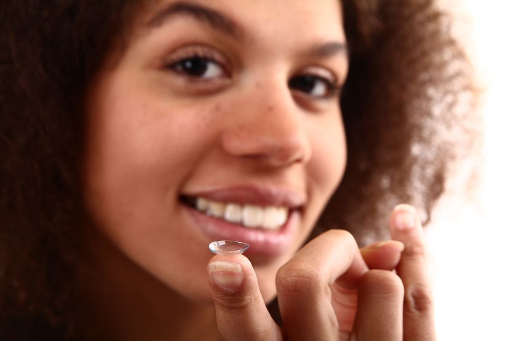 Smiling person holding a contact lens near their eye