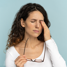 Woman holding glasses and rubbing her eye against a light blue background