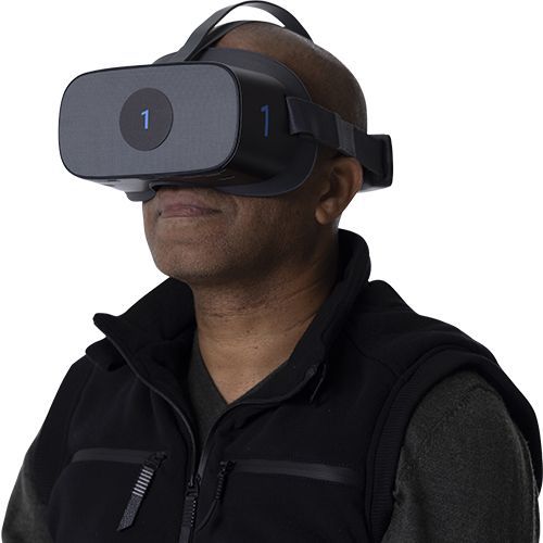 Person wearing a gray VR headset and black jacket against a plain background