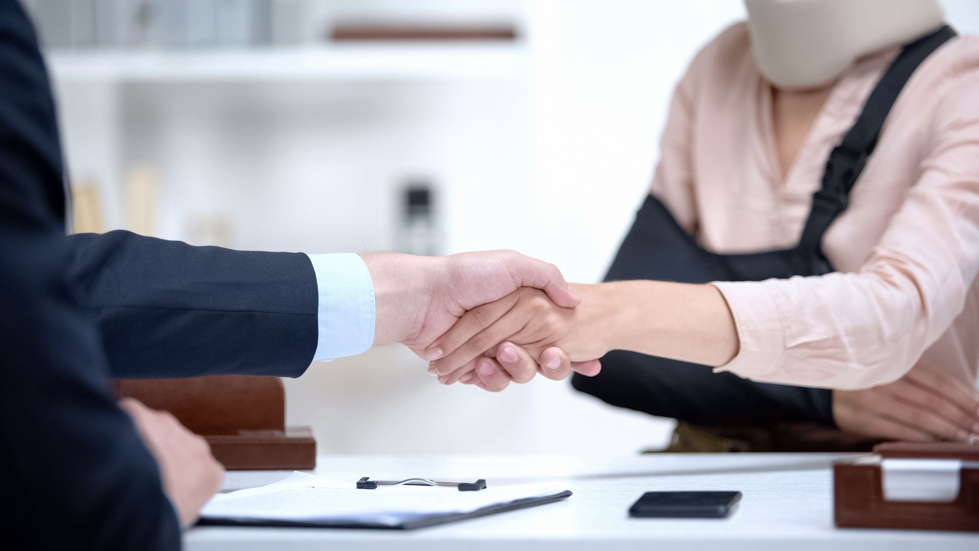 Insurance agent shaking hands with woman in arm sling.