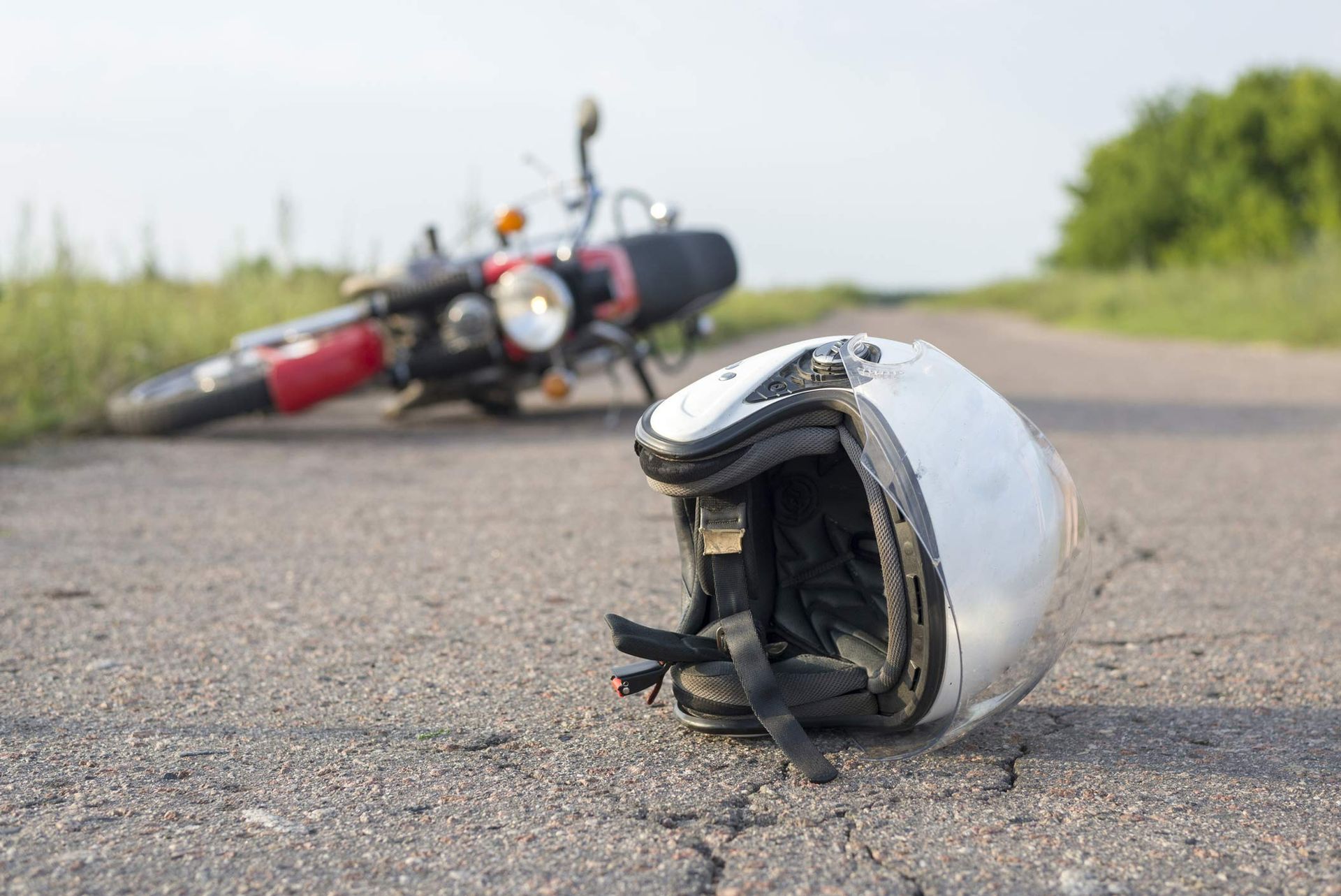 Close-up of a white motorcycle helmet on a road, with a blurry bike on the background.