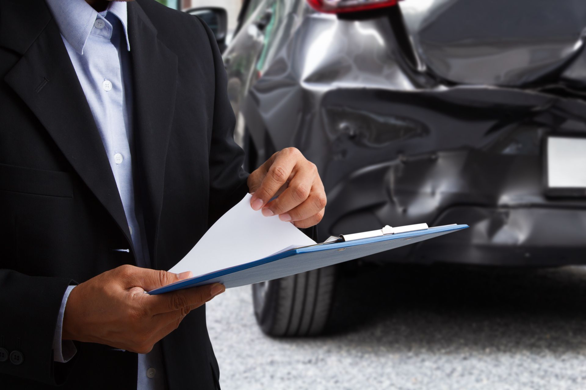 Trucking accident attorney reviews damage report in front of rear-ended vehicle with clipboard. 