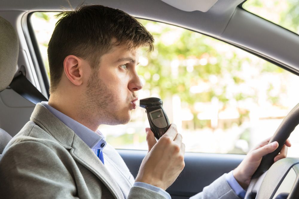 A Man Is Sitting In A Car Taking A Breathalyzer Test — Tim Warren Auto Airconditioning & Electrical In Bowen, QLD