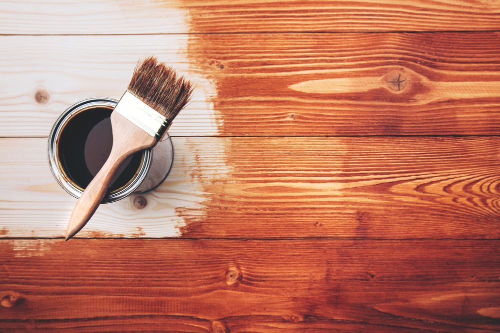 A can of paint and a brush on a wooden table.