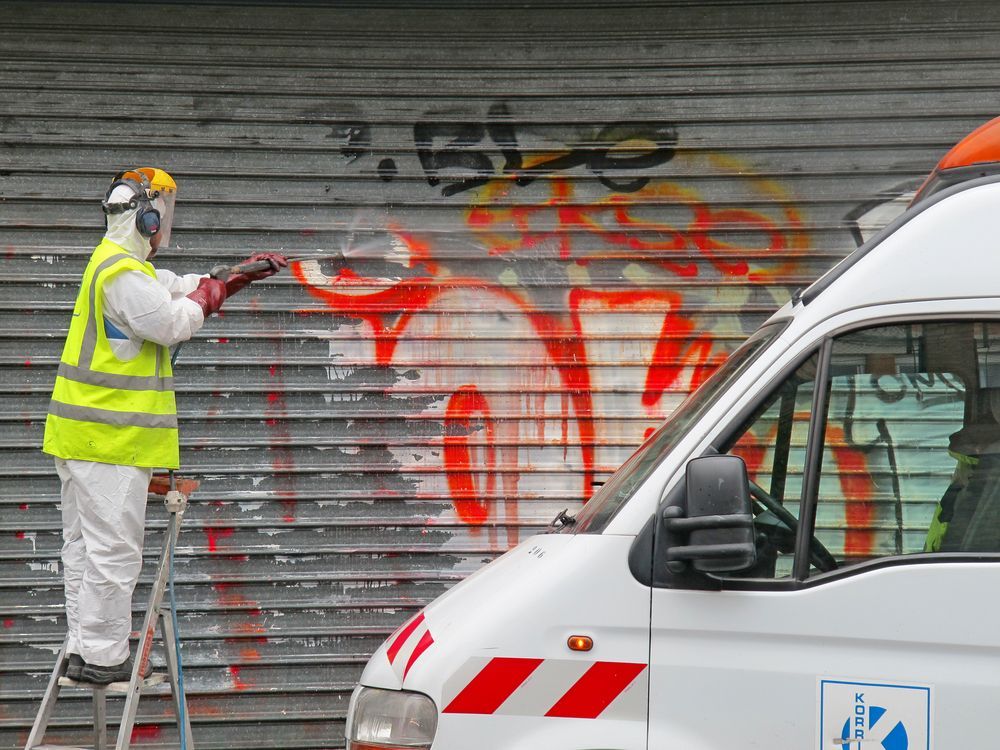 A man is spray painting graffiti on a garage door next to a white van.