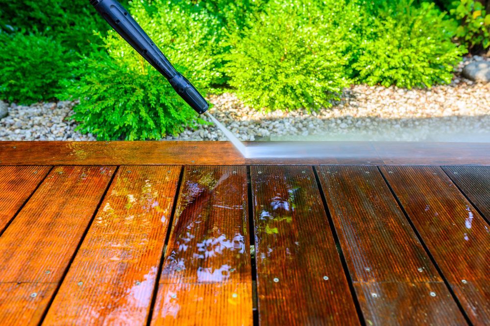 A person is using a high pressure washer to clean a wooden deck.