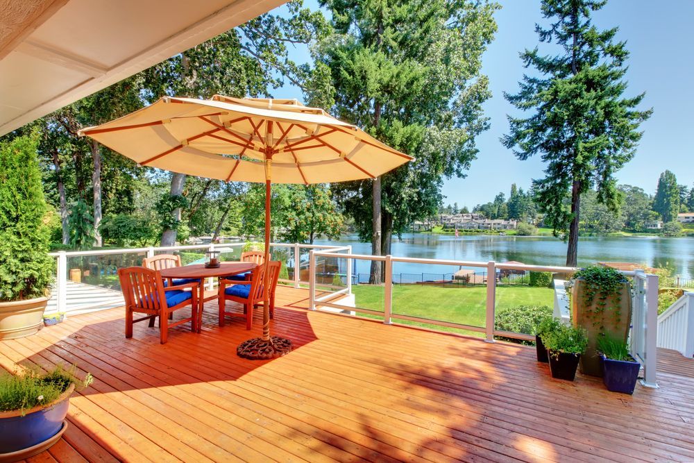 A wooden deck with a table and chairs and an umbrella overlooking a lake.