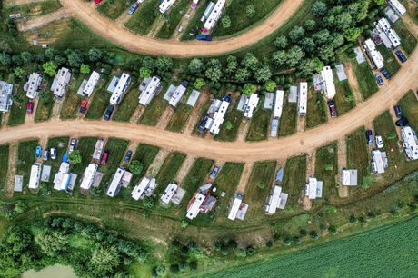 Aerial view of RV park with rows of trailers on grassy lots, dirt roads, and trees.