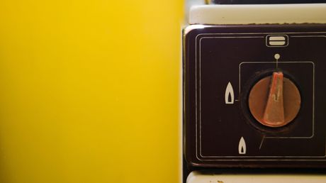 Brown stove knob with red indicator on a dark background, against a yellow wall.