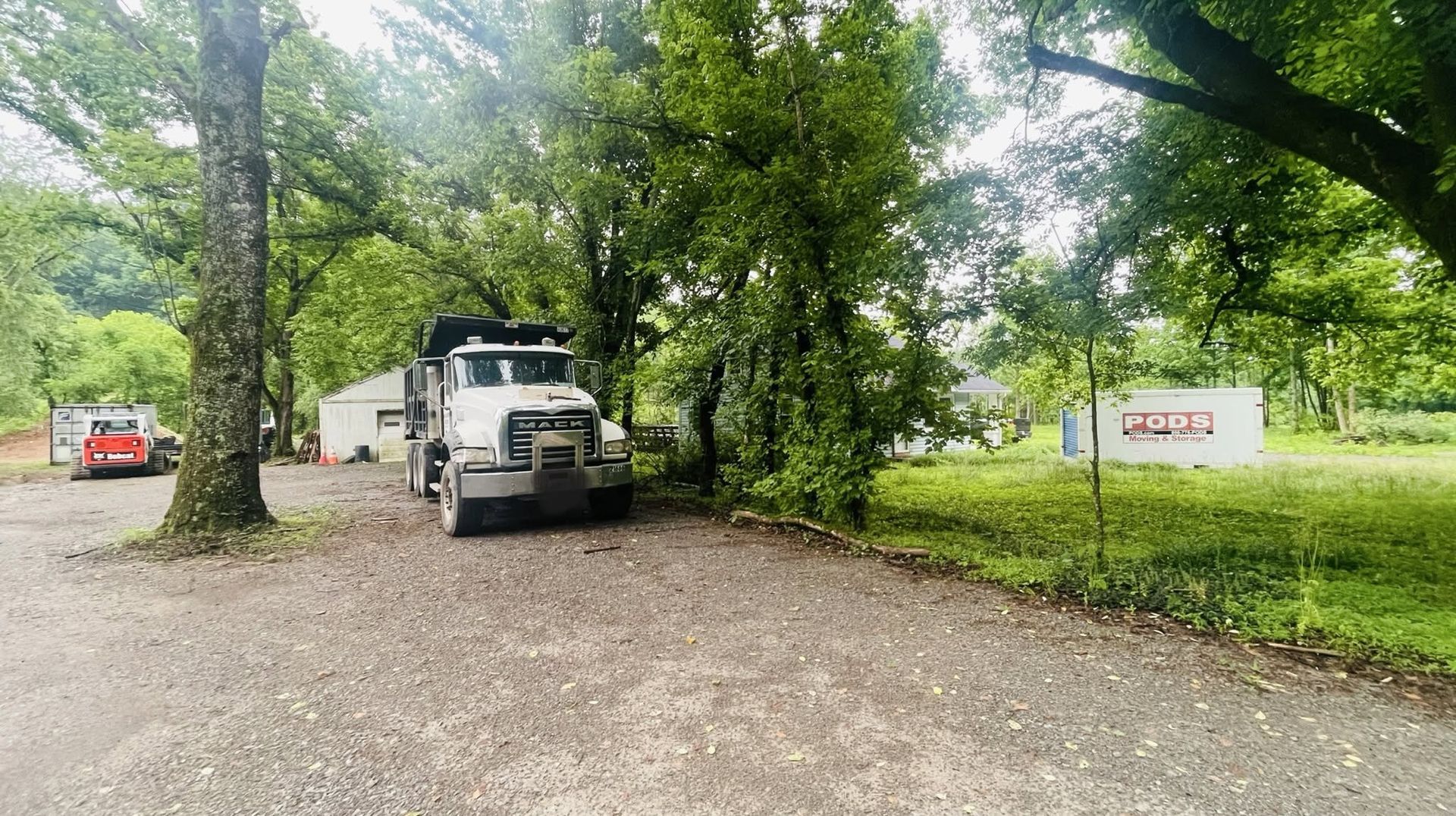White utility truck parked on a gravel driveway by trees and grassy field, with signs at both sides.