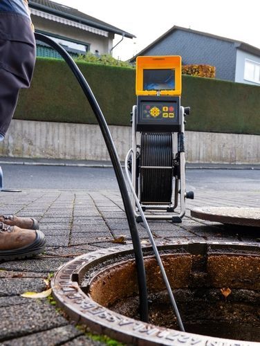 Cable-winding machine at a manhole on a residential street, with a hose or cable feeding into the opening.