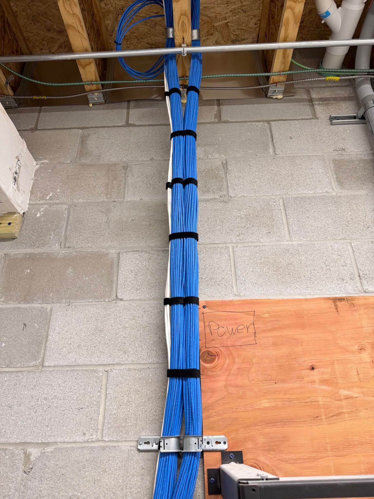 Blue cable bundle secured with black ties along a wall and floor, beside a metal conduit and orange panel cover