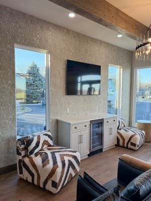 Modern living room with wall-mounted TV, white console, two patterned chairs, and tall windows with lake view