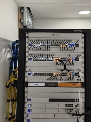 Network wiring panel with rows of connected cables and patch cords in a utility closet.