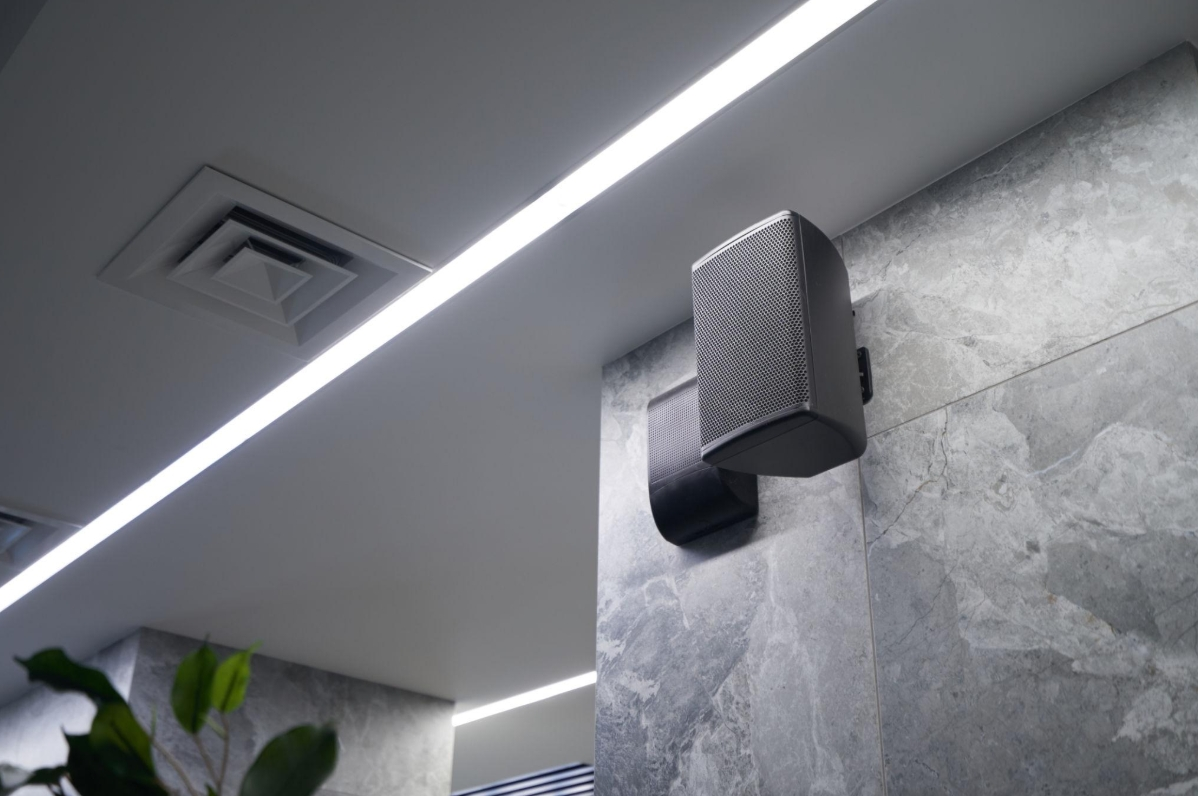 Wall-mounted speaker on a gray tiled wall beside a ceiling light strip and vent in a modern interior