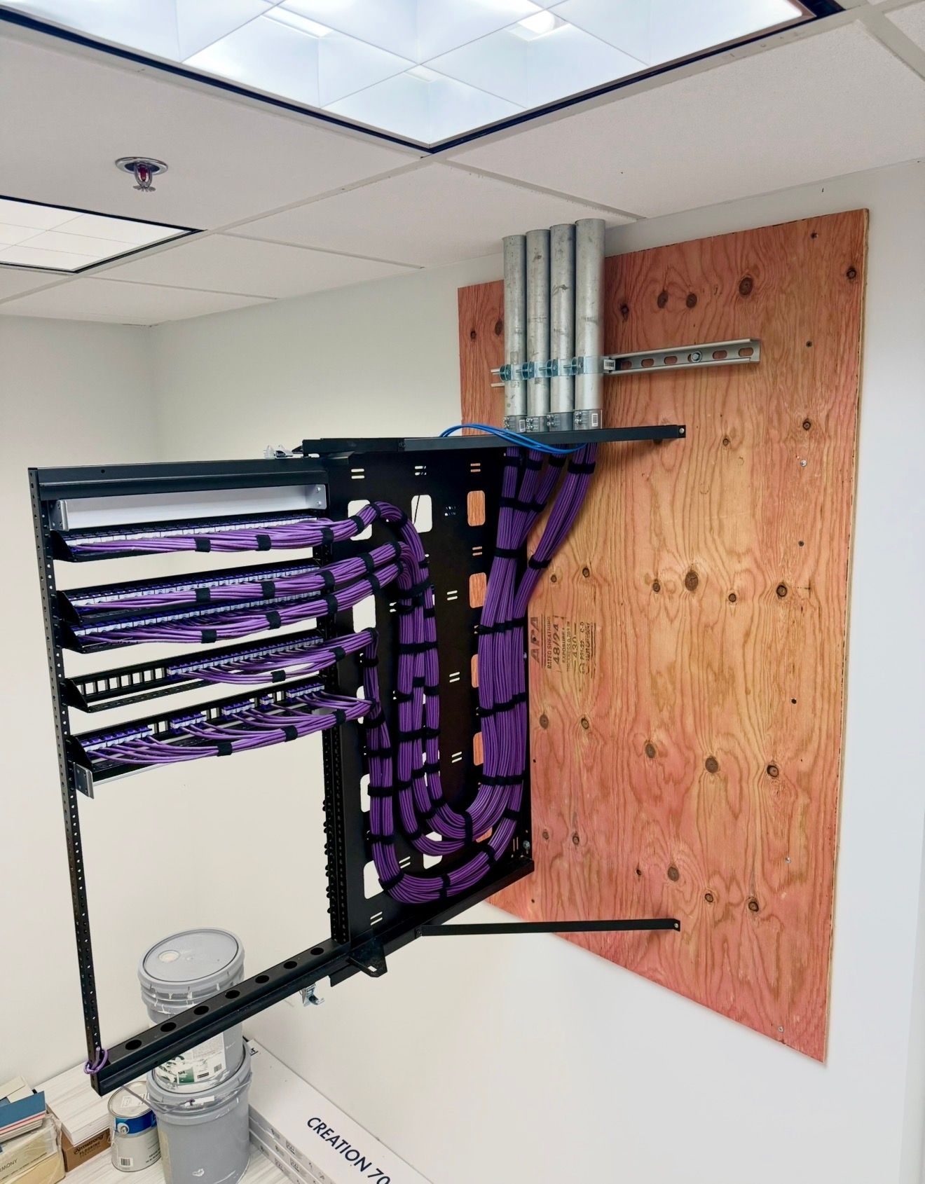 Wall-mounted network cable rack beside plywood backboard in a ceiling utility room