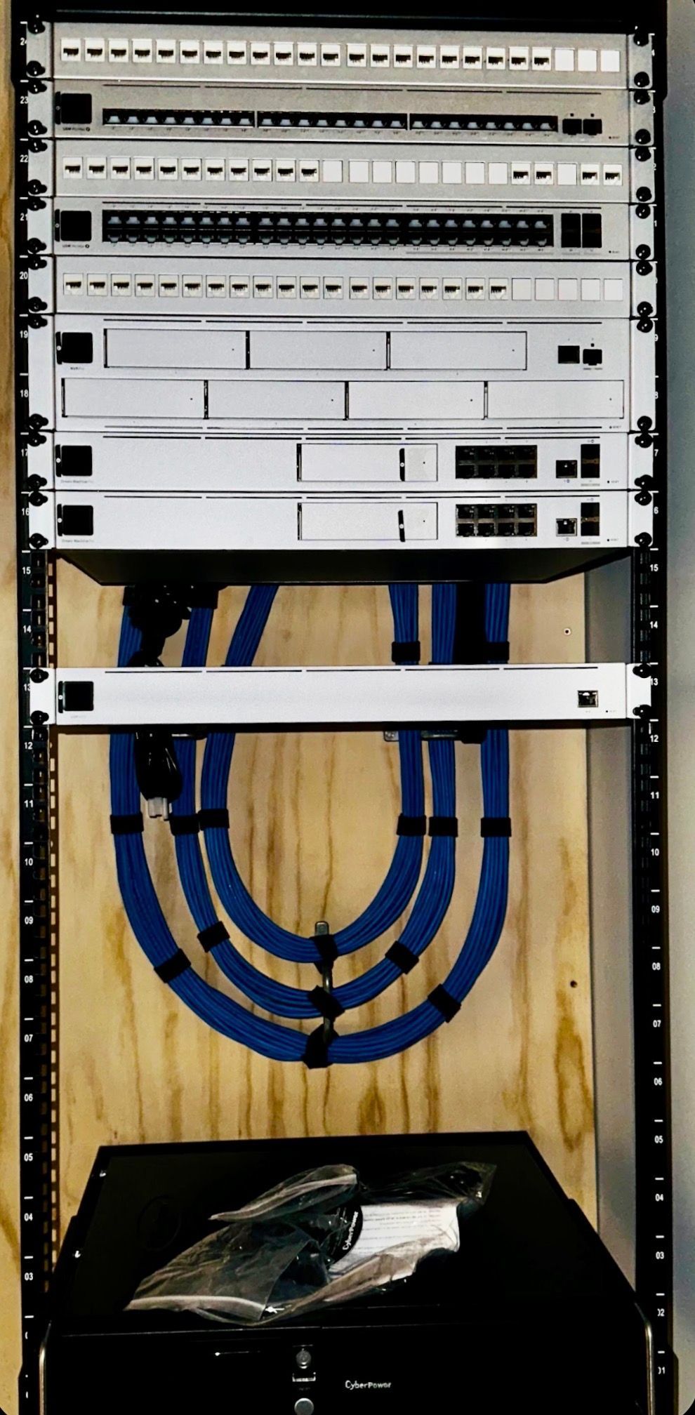Open network rack with patch panels and blue cables inside a wooden cabinet