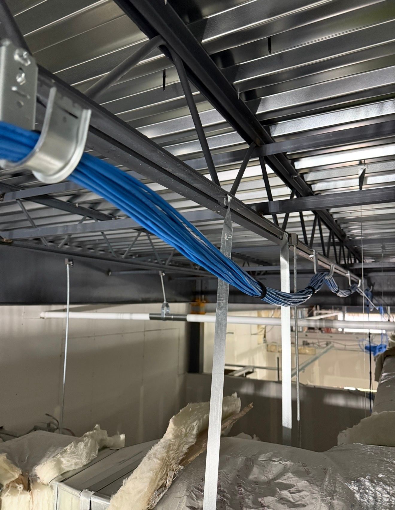 Industrial ceiling with blue cables, metal ductwork, and exposed structural beams above a construction area
