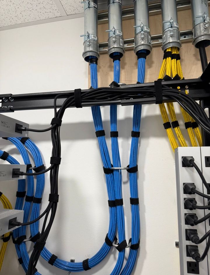 Blue and yellow network cables routed through a wall-mounted patch panel and cable management tray