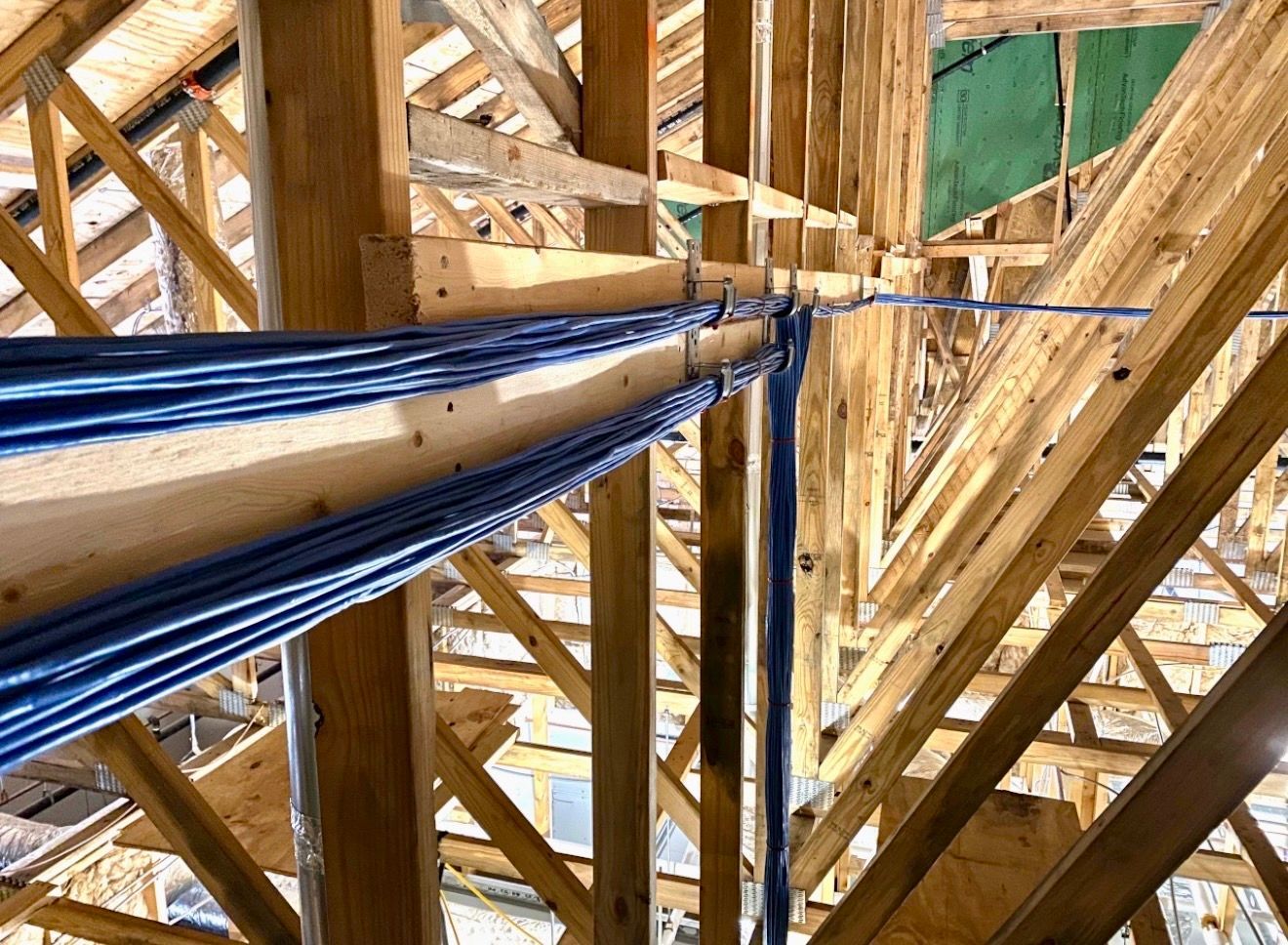 Close-up of wooden roof trusses with blue cables running through the frame during construction