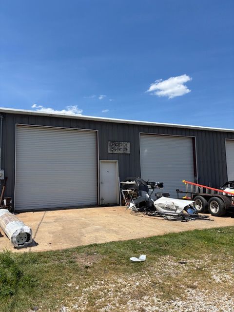 Industrial building with two roll-up doors and scattered construction debris outside under a blue sky