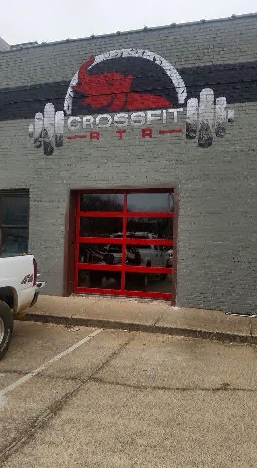 Gray CrossFit gym exterior with red garage-style door and logo sign above entrance