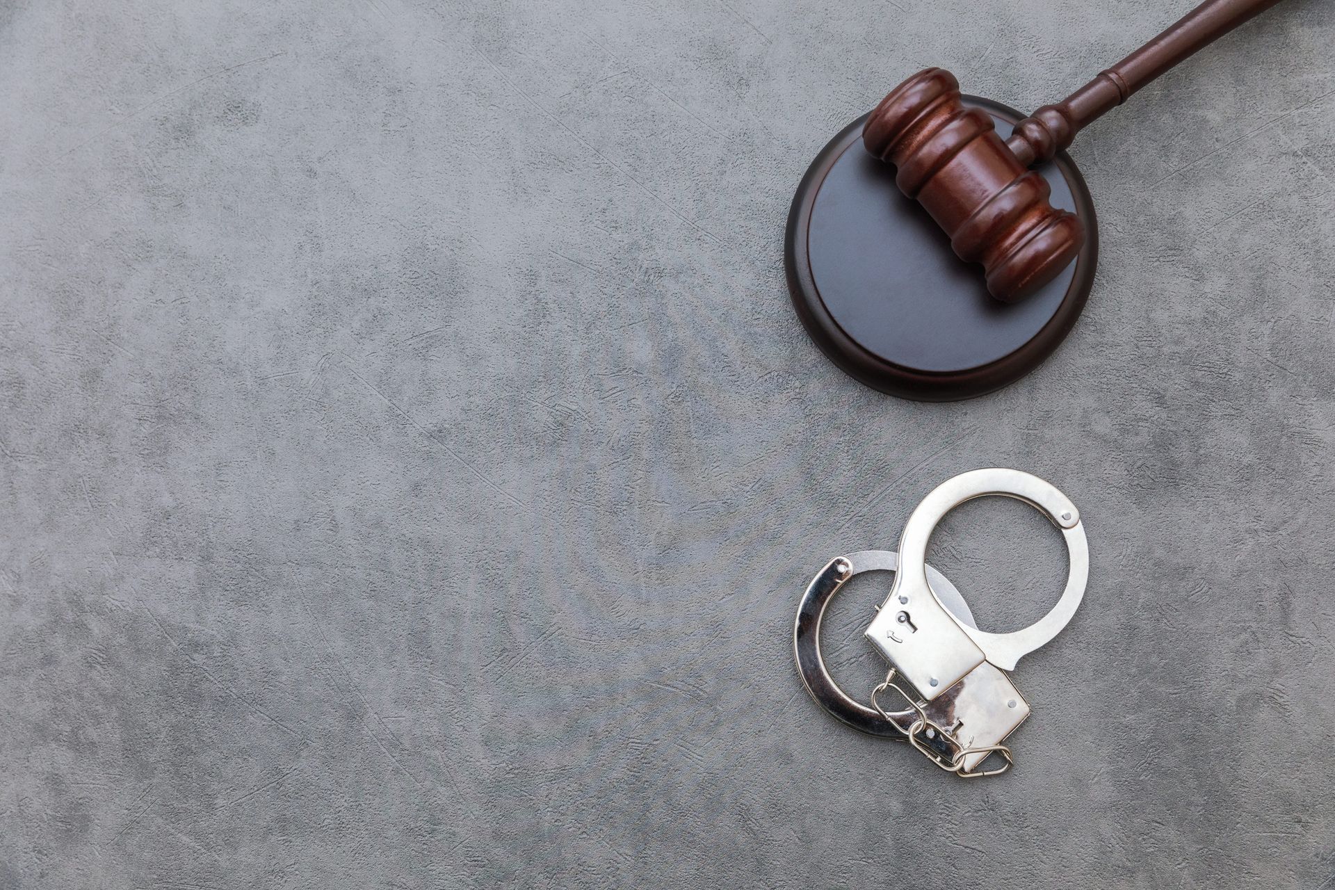 Handcuffs beside a judge’s gavel on a gray surface