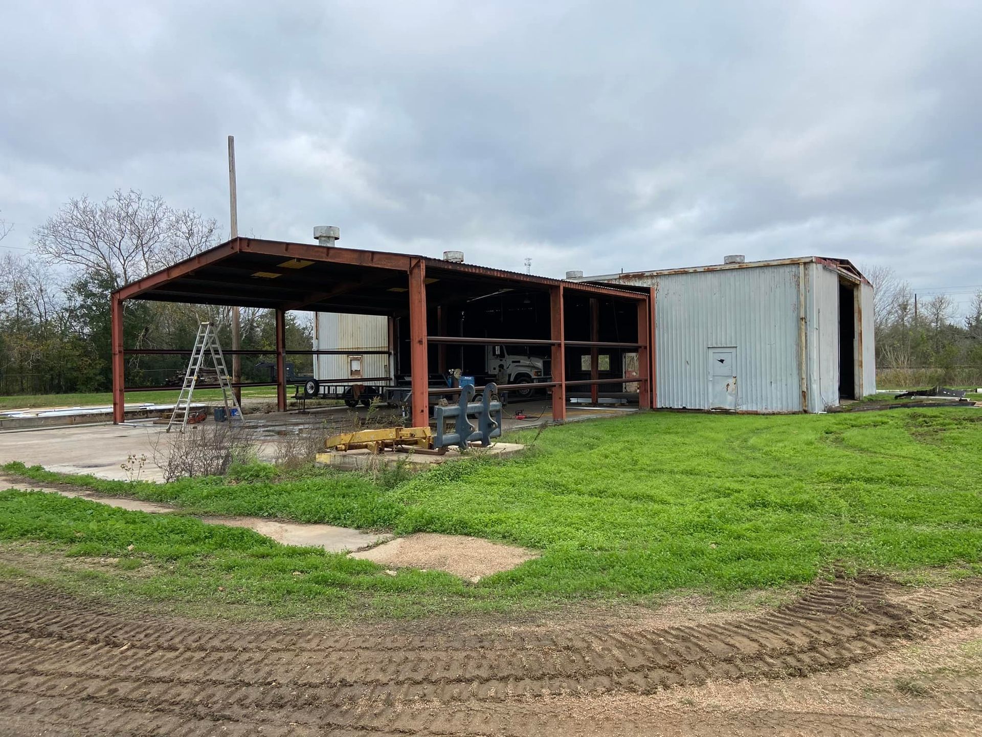 Dilapidated metal shed with a red-framed overhang on a grassy area under a cloudy sky.