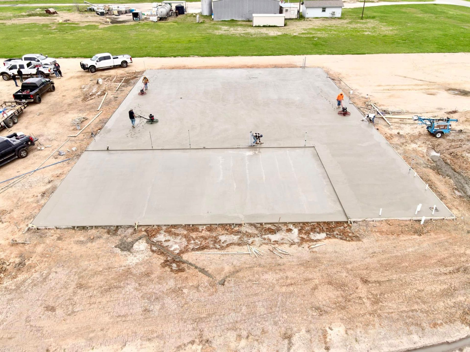 Construction site with workers smoothing a large concrete slab outdoors.