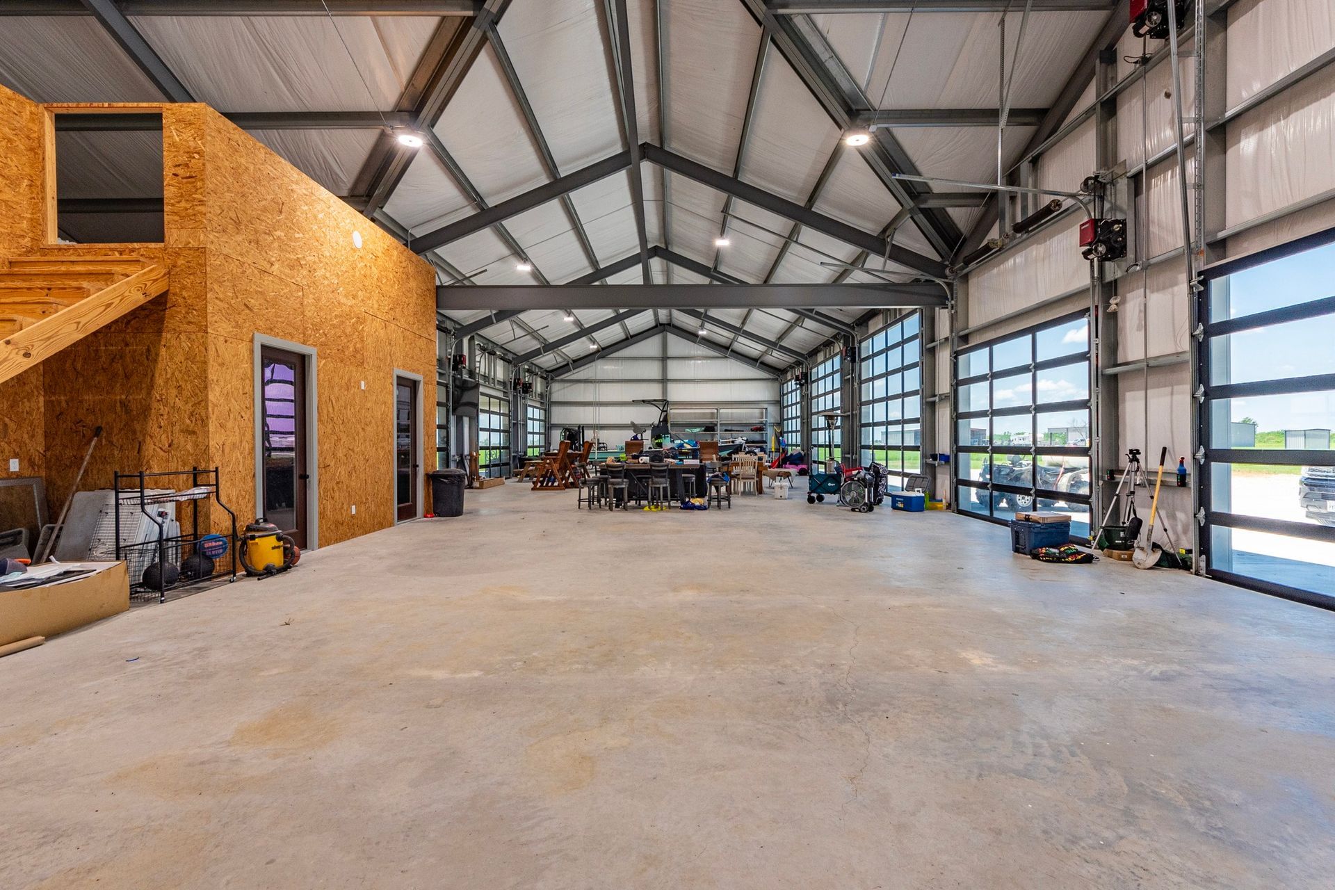 Large open workshop with concrete floor, metal frame, and glass garage doors.