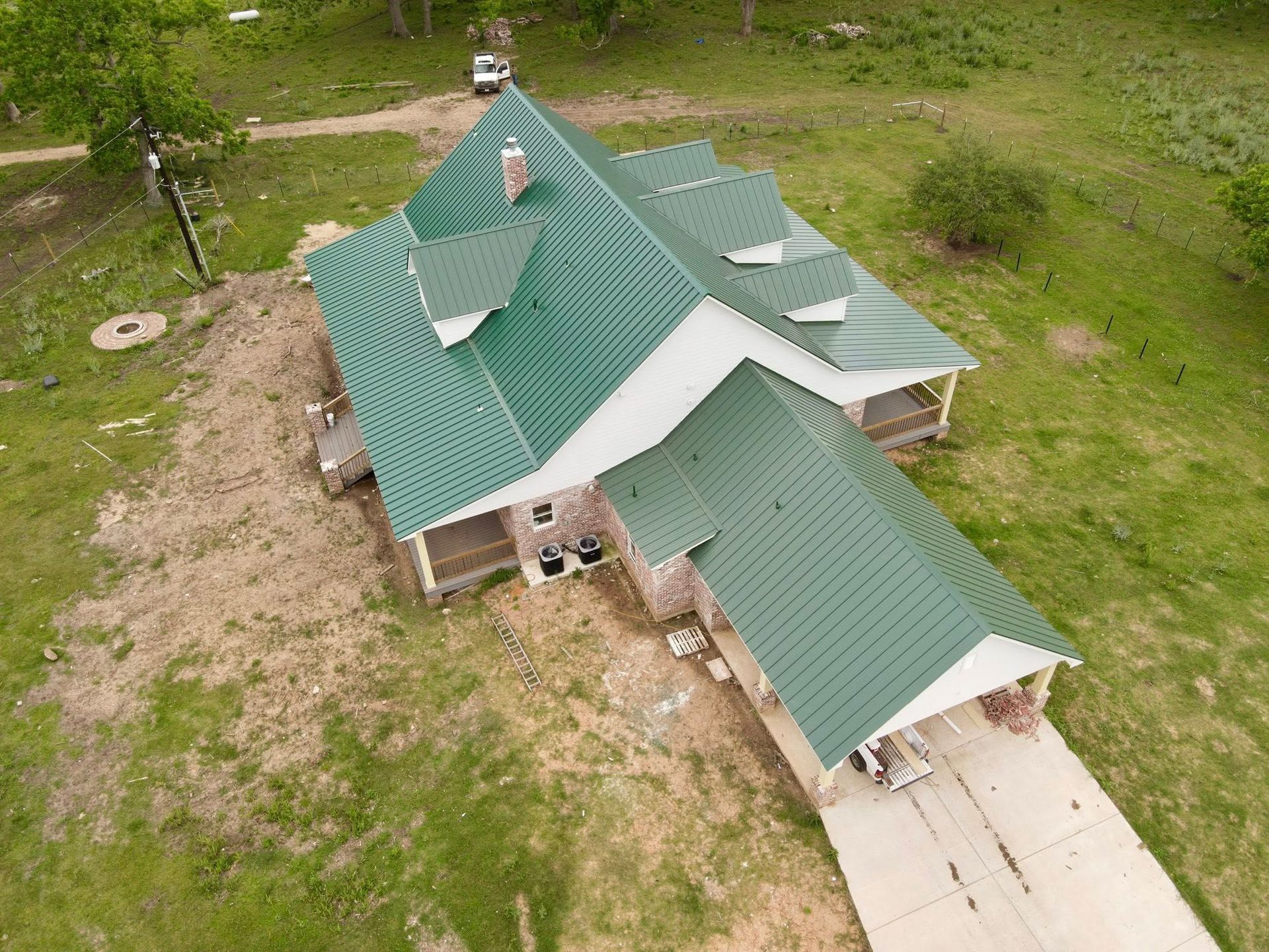 Green-roofed house with attached garage, surrounded by dry grass and a concrete driveway.