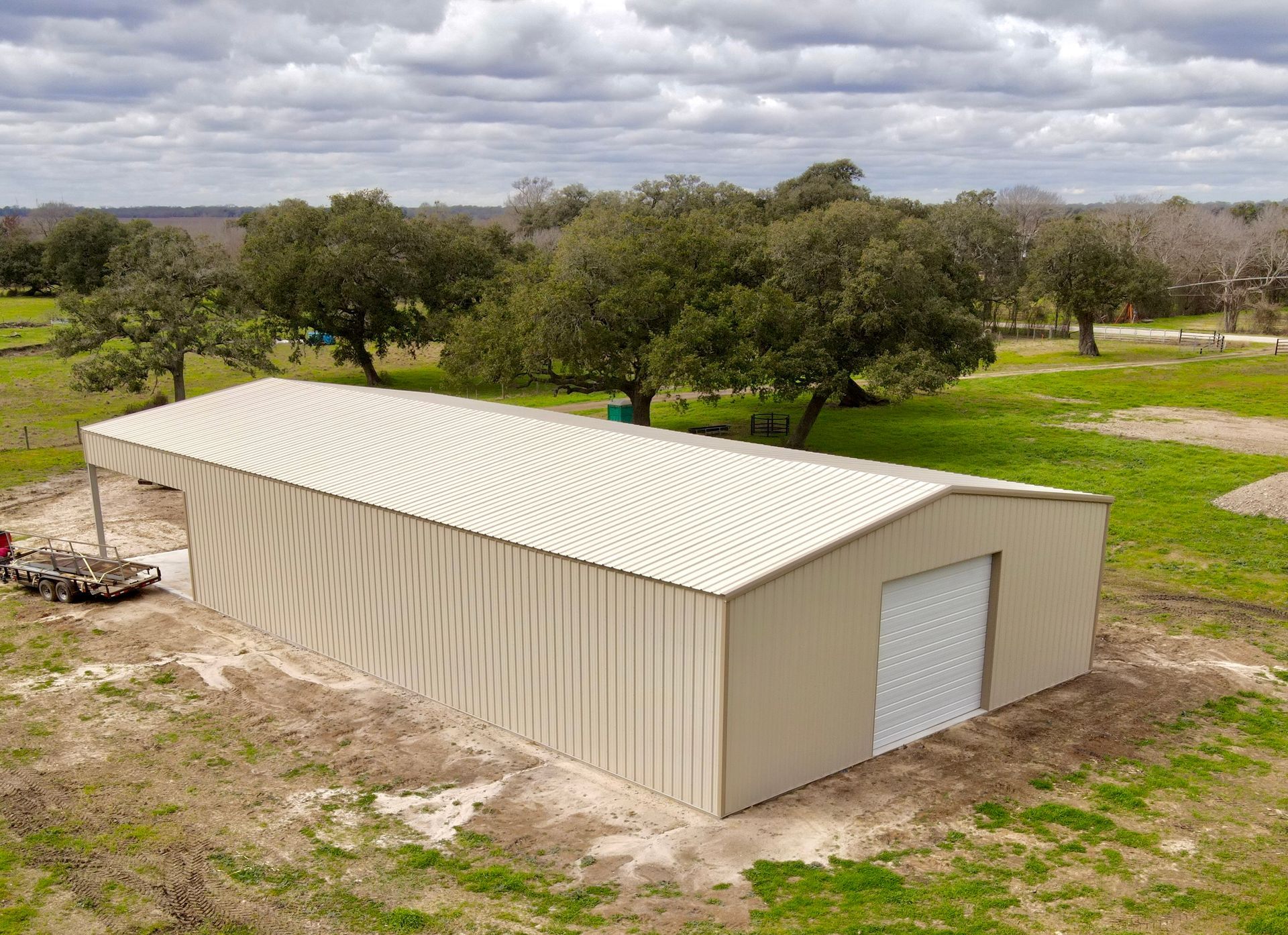 A light tan metal barn in a field, with a white door, overcast sky, and trees in the background.