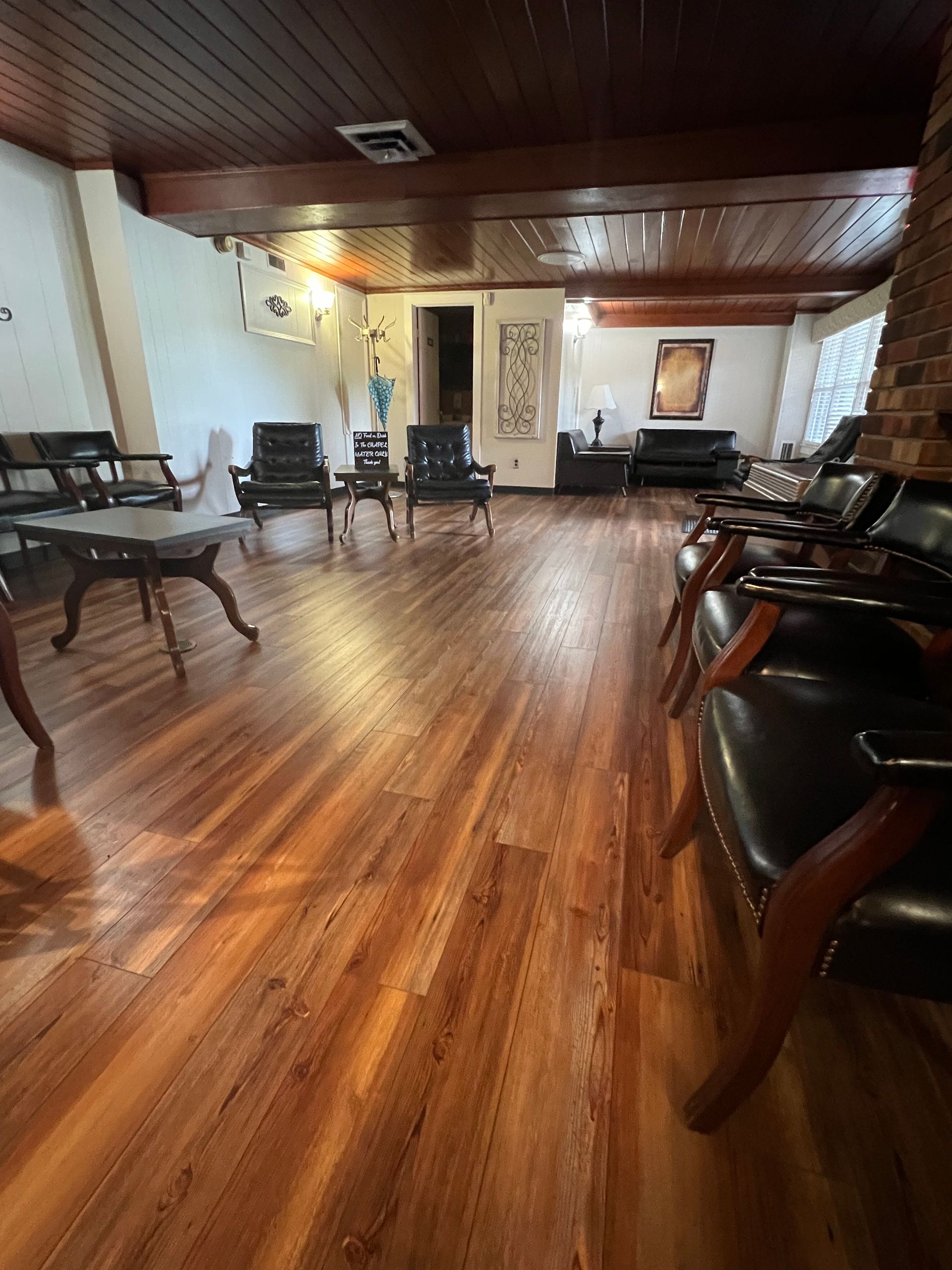 Spacious lounge with wooden floors, leather chairs, and tables under warm ceiling lights