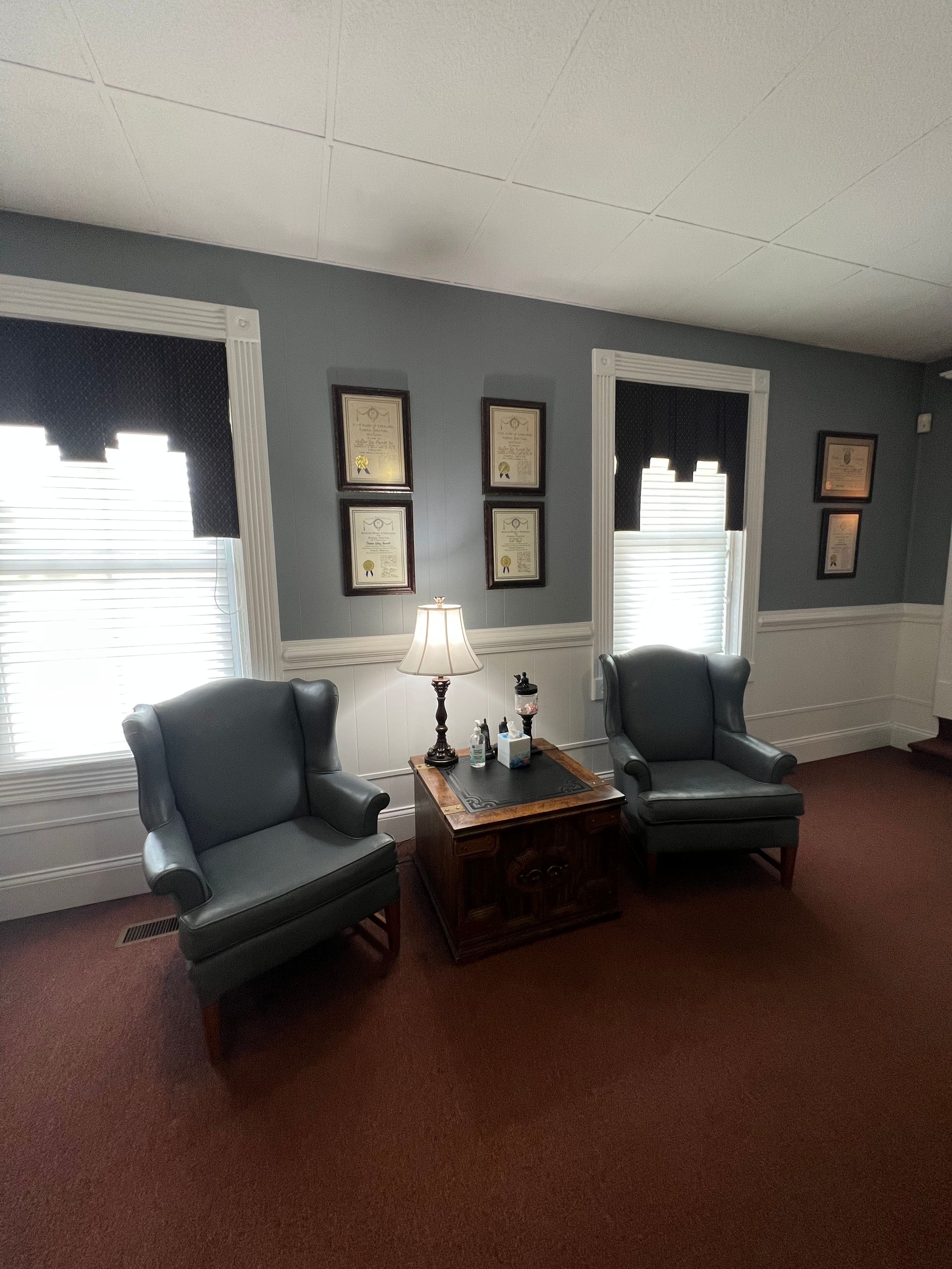Cozy sitting room with blue walls, two chairs, a small table lamp, and framed wall art