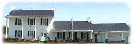 White colonial-style house with black shutters and a long porch under a clear blue sky
