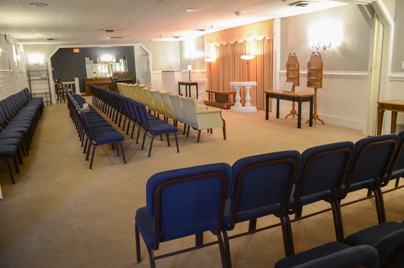 Empty meeting room with rows of blue chairs facing a small stage and lectern under warm lights