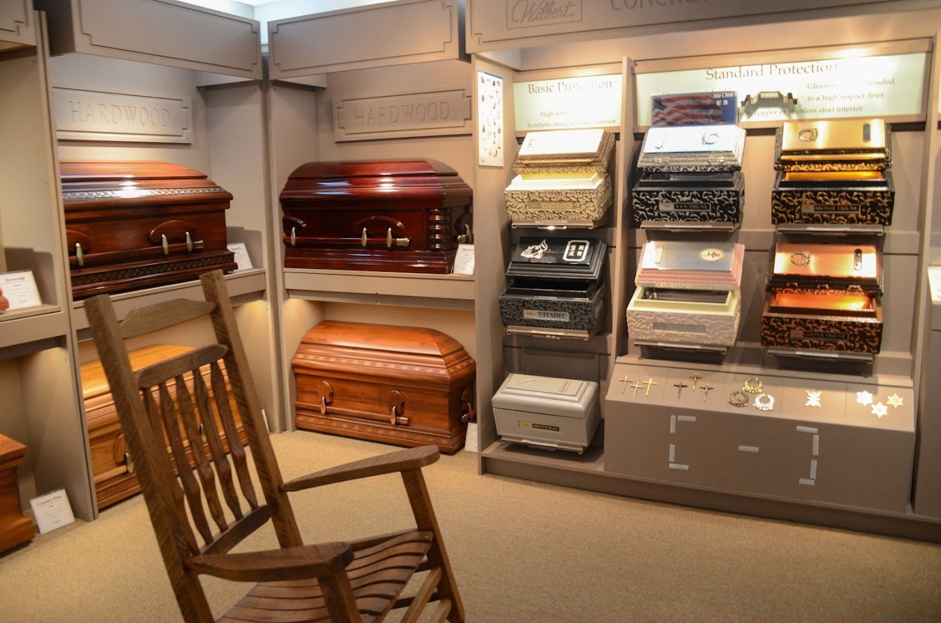 Display of decorative coffins and caskets in a showroom, with a wooden rocking chair in the foreground.