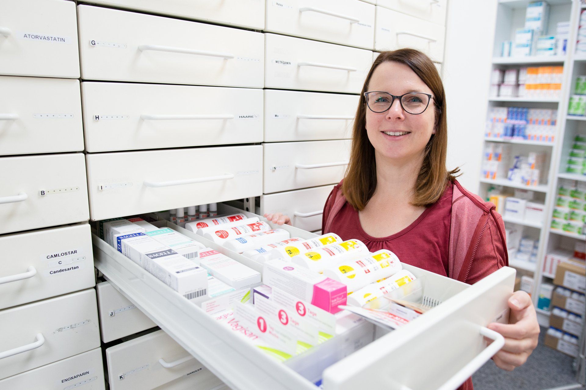 Eine Person in einer Apotheke öffnet eine Schublade, die mit verschiedenen Medikamentenschachteln und -behältern gefüllt ist.