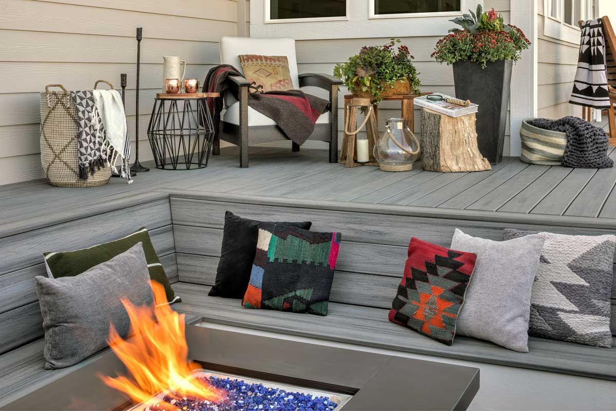 Trex® Decking from Budget Home Supply Colorado - Outdoor seating area with a gray deck, a fire pit, and various pillows, blankets, and potted plants.